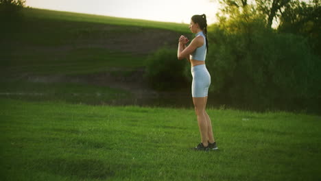 The-camera-follows-a-female-athlete-lunging-in-pairs-at-sunset.-Move-by-squatting-on-each-leg-in-turn.-General-plan-training-in-the-Park-in-the-summer